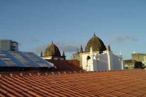 Eine Stadtansicht mit Gebäuden im Vordergrund, einem blauen Himmel im Hintergrund und Solarpanels auf einem Dach.