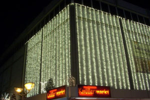 Ein festlich geschmücktes Gebäude in Berlin, Deutschland, mit Weihnachtslichtern umgeben von Bäumen, Laternenmasten und Tafeln mit Text, mit dem Himmel im Hintergrund.