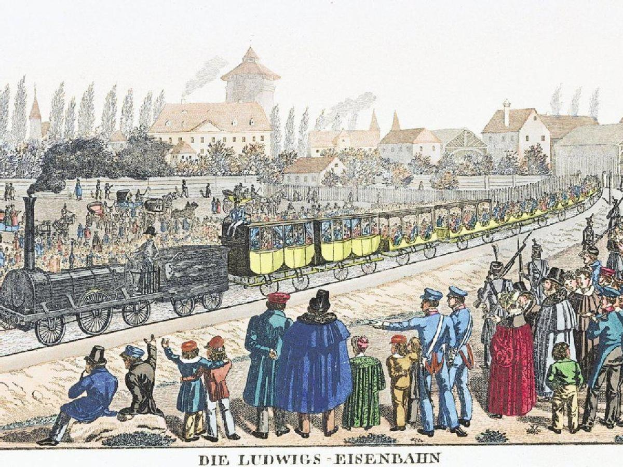 Eine Gruppe von Menschen steht um einen Zug auf einem Gleis, einige sitzen im Zug und andere stehen auf dem Boden, in der Nähe von Gebäuden und Bäumen, mit Text 'Ludwigs-Eisenbahn, die erste Bahnstation in Deutschland' unten.