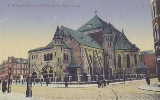 Altes Foto einer Kirche in städtischer Umgebung mit umliegenden Gebäuden, Straßeninfrastruktur, Fußgängern, Fahrzeugen, Bäumen und einem klaren Himmel, mit Text oben.