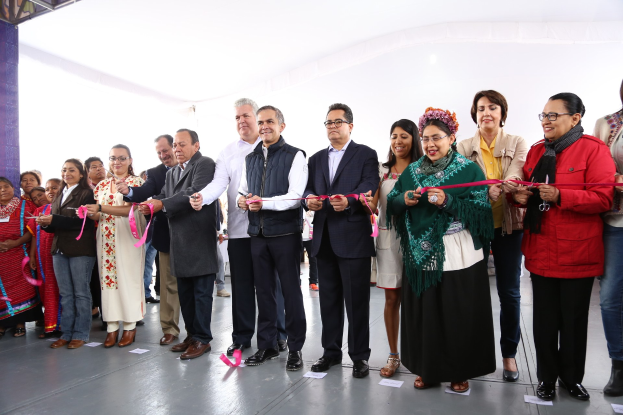 Eine Gruppe von Menschen, die eine Schnur schneiden, vor einem Publikum mit einer Säule links und Papieren auf dem Boden.