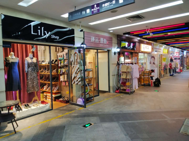 Ein Schaufenster mit Schaufensterpuppen im Fenster, Kleidung, Schuhe, eine sitzende Person, ein Tisch mit einer Tasche, ein Fernseher und ein Schild mit der Aufschrift "Lily Shop."