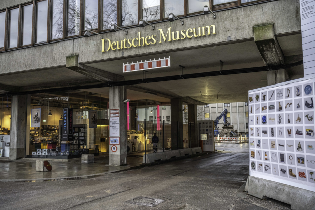 Außenansicht des Deutschen Museums in Berlin: großes Glasgebäude mit Säulen, Namensschild und Informationsdisplay auf der rechten Seite, Bäume und andere Gebäude im Hintergrund.