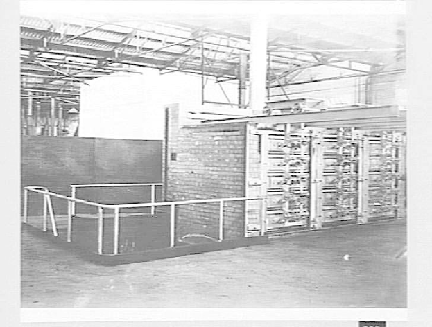 Schwarzes und weißes Foto eines großen Raums mit einem Supercomputer in der Mitte, einer Wand im Hintergrund, einem Boden unten und einer Decke mit Stangen oben.