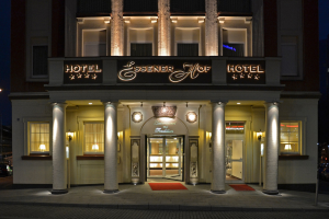 Das Essener Hof Hotel in Berlin, Deutschland, mit einem Geb├Ąude mit Fenstern, Türen, S├Ąulen, Lichtern und einem Namensschild, das sich entlang einer Stra├če mit Fahrzeugen auf der rechten Seite und dem Himmel im Hintergrund befindet.