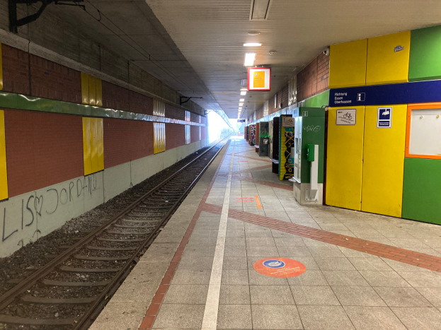Ein Bahnhof in Berlin, Deutschland, mit einem Zug auf den Schienen, beleuchtet von Deckenlampen, mit Graffiti an der linken Wand und ein paar Gegenständen auf der rechten Seite.
