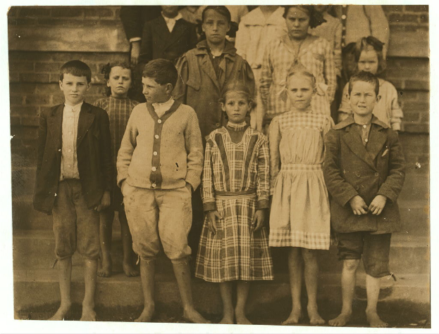 Eine Gruppe von Kindern in Schwarz-Weiß, mit einem Jungen in einem Anzug in der Mitte, vor einer Wand stehend.