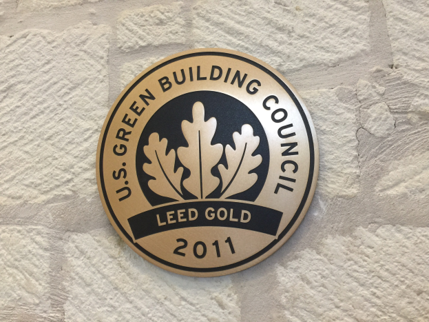 Logo der U.S. Green Building Council an einer Gebäudefassade, mit einem grünen Schild mit weißer Umrandung und schwarzer Schrift, eingerahmt von einem Lorbeerkranz.