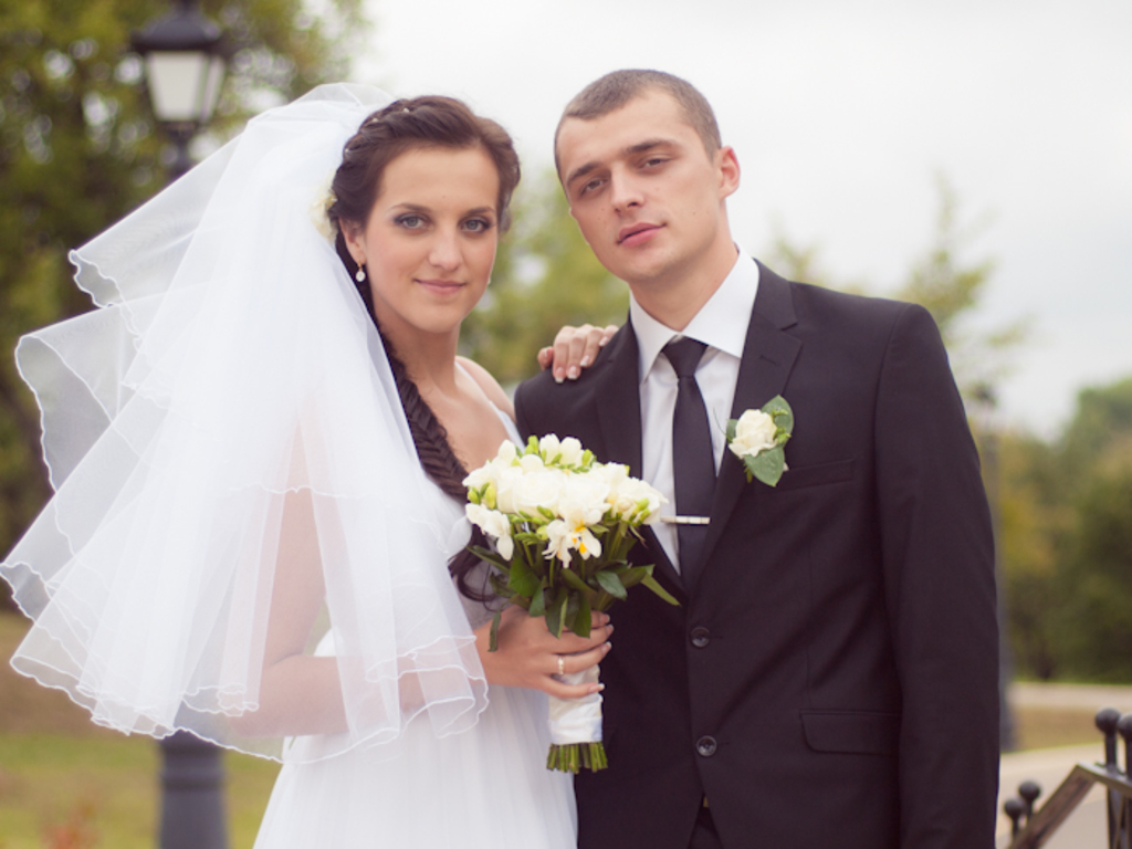 Ein Mann und eine Frau in Hochzeitskleidung stehen zusammen, die Frau hält Blumen in den Händen.