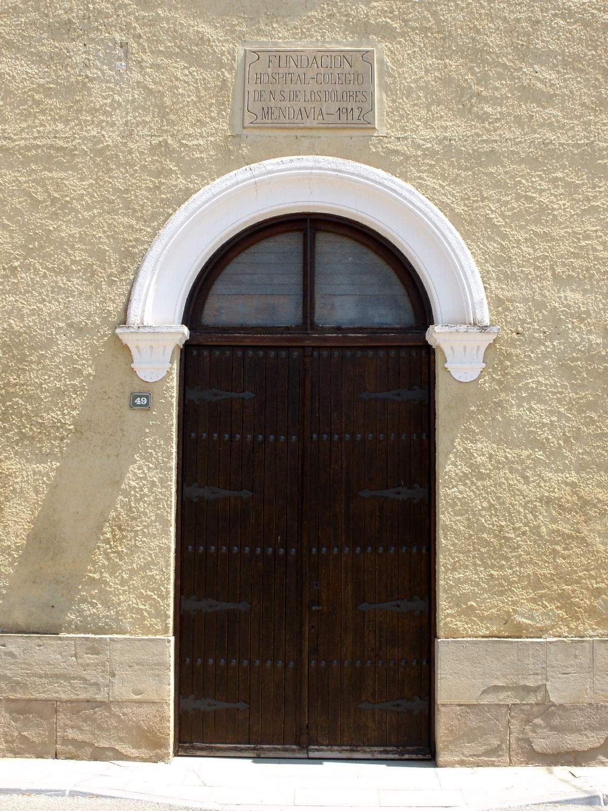 Alte hölzerne Tür mit einem Namensschild darüber, wahrscheinlich der Eingang zu einem Krankenhaus, in einem steinernen Gebäude mit einer Straße unten.