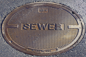 Metallschachtdeckel auf der Straße mit dem Wort "Kanal" darauf.