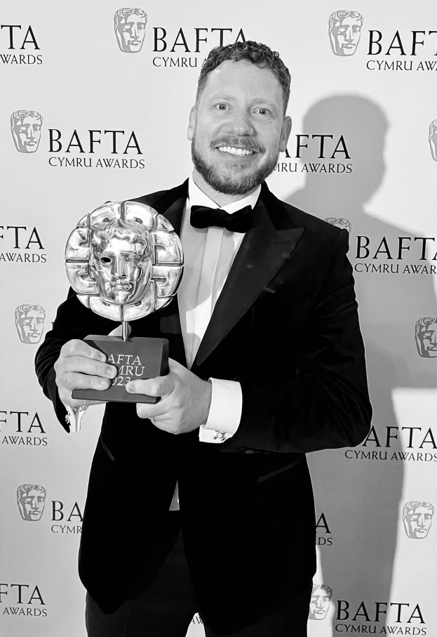 Ein Mann in einem Smoking, der eine BAFTA-Trophäe hält und lächelt, mit 'BAFTA Awards 2018' im Hintergrund.
