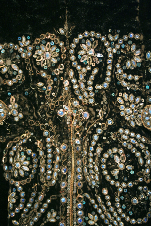 Ein Close-up eines schwarzen Kleides mit aufwendiger blauer und goldener Stickerei, das Luxus und Eleganz ausstrahlt.