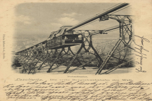 Ein altes Schwarz-Weiß-Foto einer Eisenbahnbrücke mit einem Kran, umgeben von Bäumen und einem bewölkten Himmel, mit Text unten lesend "Bahnstrecka, die erste Eisenbahnbrücke in Deutschland".