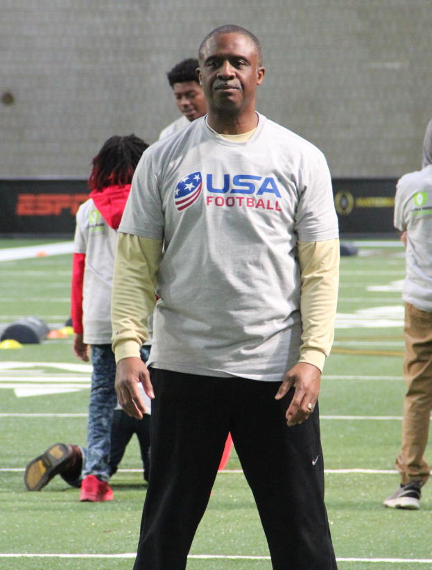 Ein Fußballspieler auf einem Feld mit einer Gruppe von Menschen und einer Wand im Hintergrund.