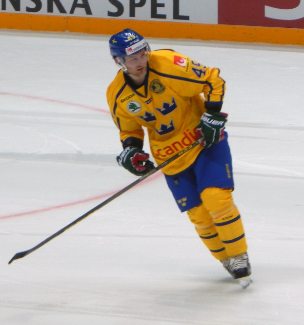 Eishockeyspieler in Bewegung auf dem Eis, der einen Helm, Handschuhe und Schlittschuhe trägt und einen Hockeystock hält, mit einem Hintergrundboard mit Text.