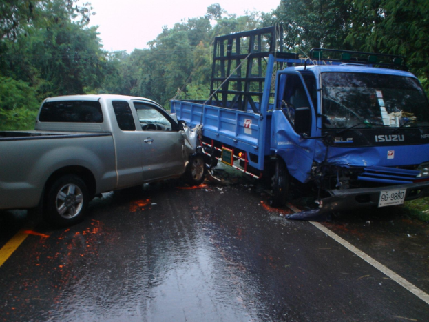 Ein schwerbeschädigter Lkw mit eingedellter Frontpartie und verbeulter Karosserie am Straßenrand, umgeben von Bäumen unter einem klaren blauen Himmel.