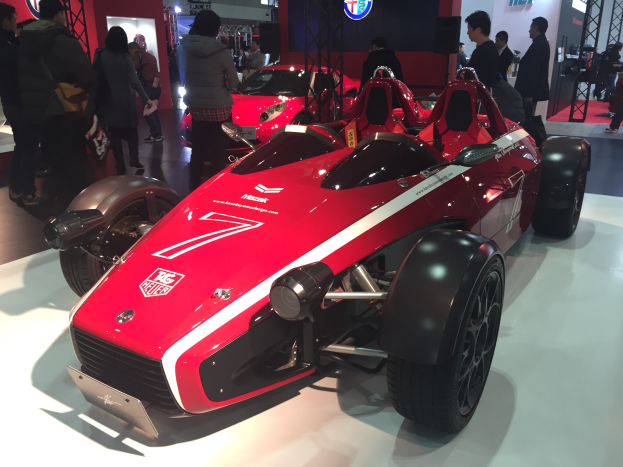 Ein rotes und schwarzes Auto auf der Shanghai Auto Show umgeben von Menschen und verschiedenen Gegenständen im Hintergrund.