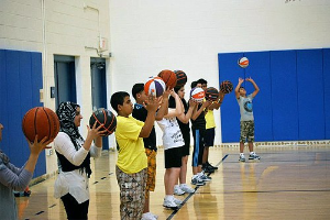 Gruppe junger Menschen mit Basketballs auf einem Platz, mit Türen und einer Wand im Hintergrund.