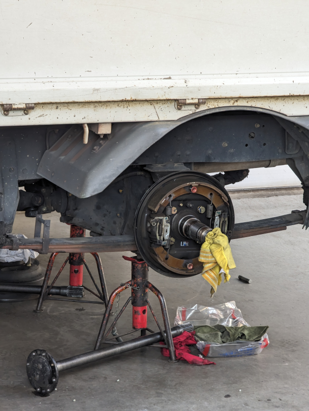 Ein Lkw in einer Garage geparkt, mit einem gelben Tuch darüber, umgeben von verstreuten Werkzeugen und Gegenständen auf dem Boden.