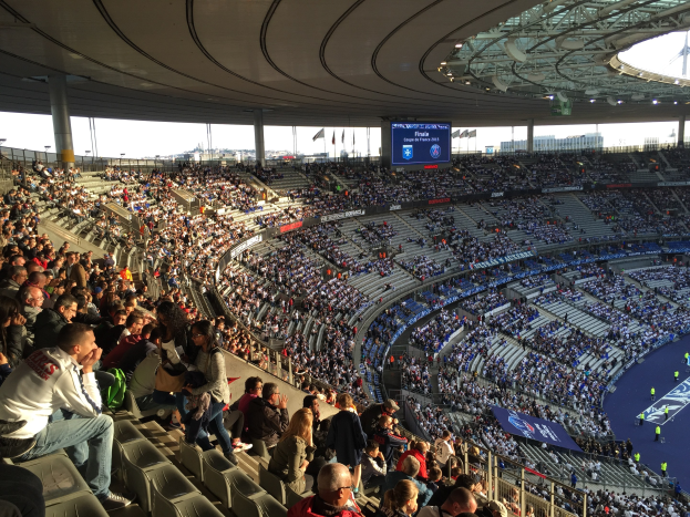 Gro├če Menge in einem Stadion bei einem Fussballspiel mit einer Bühne, Fahnen und einem Hintergrundbild, identifiziert als Allianz Arena in München, Deutschland.