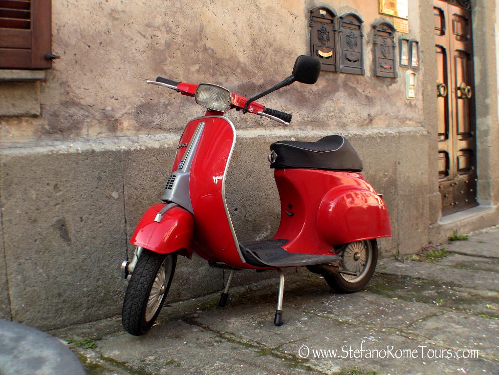 Ein roter E-Scooter steht vor einem Haus mit Tür und Fenstern auf einer Straße mit sichtbarem Text.