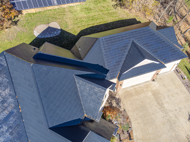 Ein Haus mit Solarmodulen auf dem Dach, umgeben von Bäumen, Gras und einem Zaun, von oben betrachtet.
