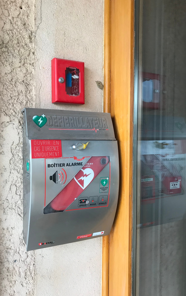 Eine rote Feueralarmanlage mit einer Glastür auf der rechten Seite, die an der Seite eines Gebäudes montiert ist und als Defibrillator fungiert, um die Menschen auf mögliche Brandgefahren aufmerksam zu machen.