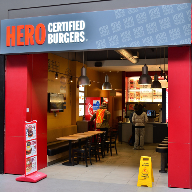 Ein Restaurant von Hero Certified Burgers in London mit Kunden, Tischen, Stühlen, einer Speisekarte, einem Wandfernseher und Deckenleuchten.