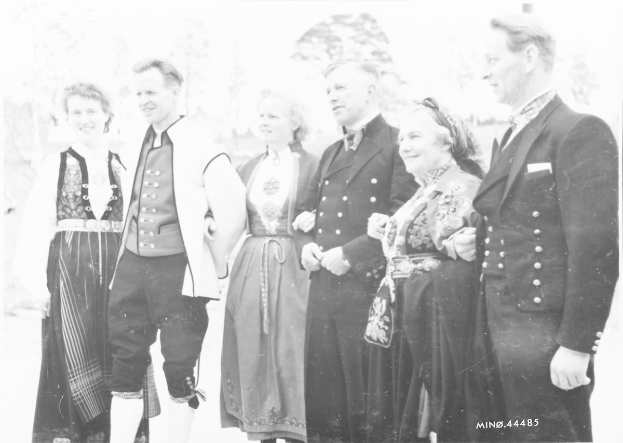 Eine Gruppe von Menschen in den 1930er Jahren, die zusammenstehen, lächeln und im Hintergrund Bäume zu sehen sind, mit dem Text "Bayerische Familie in den 1930er Jahren" unten.