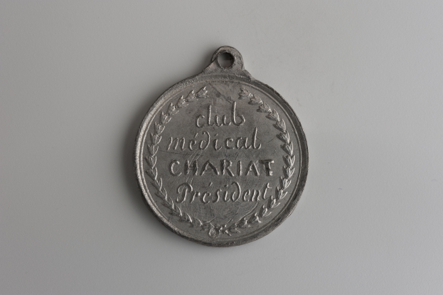 Eine Silbermedaille mit der Aufschrift "Club Medical Charity President" auf einem weißen Hintergrund.