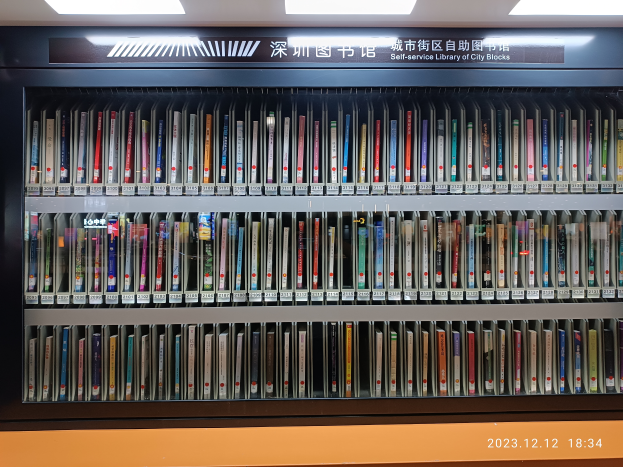 Eine Bibliothek mit Regalen voller Bücher, beleuchtet von Deckenlampen, mit einer Texttafel und einem Wasserzeichen unten, sieht aus wie eine Selbstbedienungsbibliothek von Stadtvierteln.