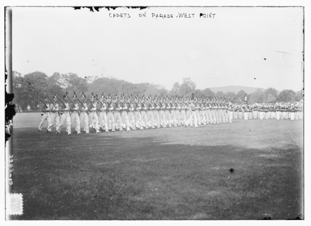 Gruppe von Menschen auf dem Boden stehend, einige halten Gewehre, mit Bäumen, Hügeln und einem bewölkten Himmel im Hintergrund; Text oben lautet "cadets on parade west point".