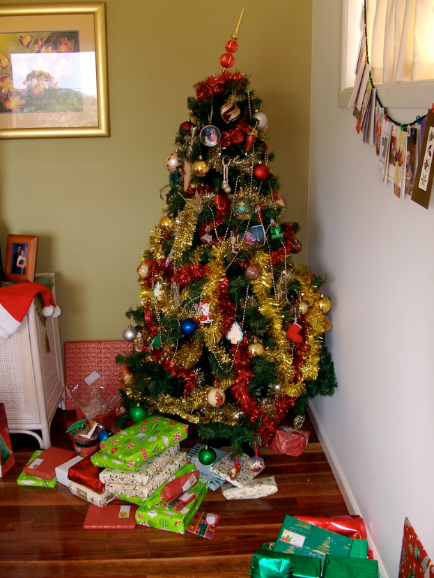 Ein geschmückter Weihnachtsbaum auf der rechten Seite mit Geschenken unten, ein Foto Rahmen an der linken Wand und ein Vorhang am rechten Fenster.