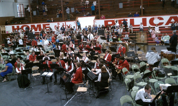 Eine Gruppe von Kindern sitzt auf Stühlen in einem Stadion während eines Musikunterrichts, wobei im Hintergrund Stadionplätze zu sehen sind.