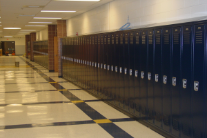Eine lange Reihe von Spinden in einem Schulflur mit einem gefliesten Boden, einer Wand im Hintergrund, einer Decke mit Lampen oben und ein paar Gegenstände herum.