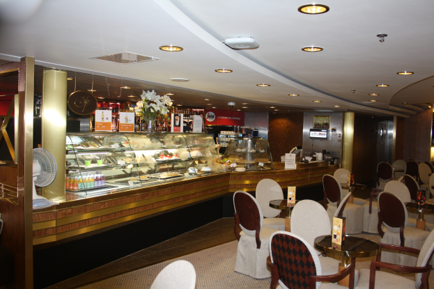 Ein Restaurant-Innenraum mit Tischen und Stühlen, einer Theke mit Blumenvasen, Schildern, einem Ventilator und anderen Gegenständen unter einer Decke mit warmer Beleuchtung.