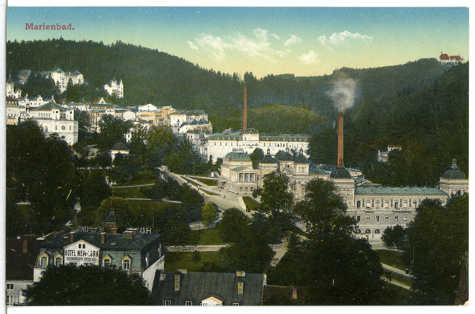 Altes Schwarz-Weiß-Foto einer Stadtlandschaft mit Gebäuden, Bäumen, Straßen, Gras, Strommasten, Rauch, fernen Hügeln und einem bewölkten Himmel, mit Text oben.