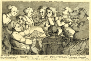 Eine Gruppe von Menschen sitzt um einen Tisch, wobei eine Person ein Buch hält, während andere in ein Gespräch vertieft sind.