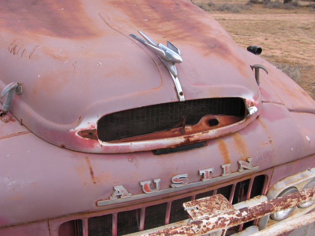 Alter rostiger Lkw auf einem Feld mit Bäumen und einem klaren blauen Himmel, der Spuren einer längeren Exposition gegenüber den Elementen zeigt.