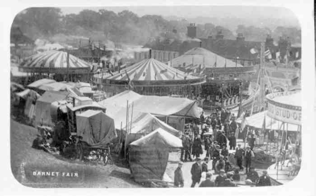 Ein altes Schwarz-Weiß-Foto einer belebten KarnevalsSzene mit Zelten, Menschen, Karren und Gebäuden im Hintergrund, beschriftet mit "Barnet Fair, London, England".